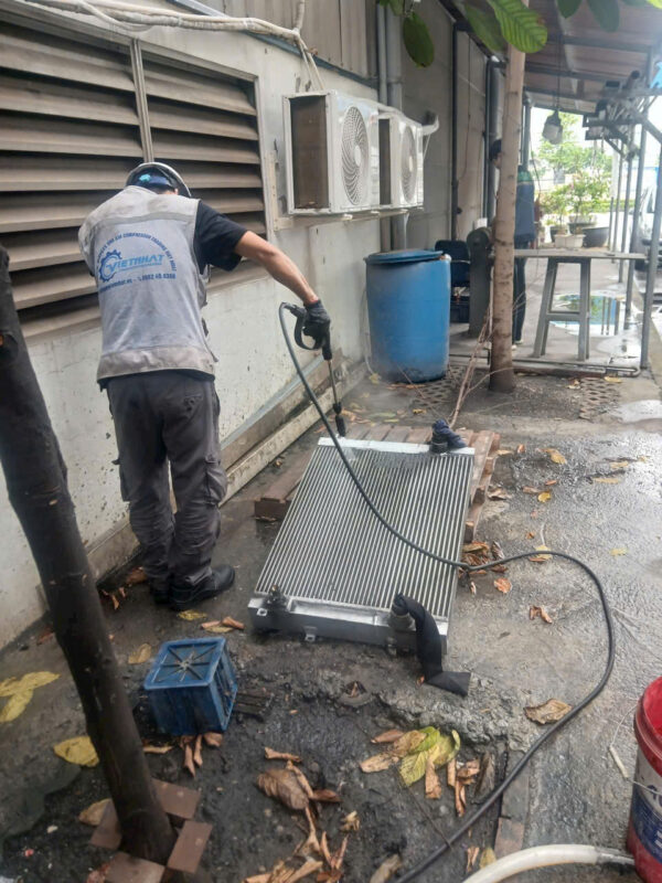 Kỹ thuật viên của Việt Nhật đang sử dụng súng phun áp lực nước để vệ sinh giàn làm mát máy nén khí trục vít, loại bỏ hoàn toàn bụi bẩn bám dính sâu trong các khe lá nhôm.